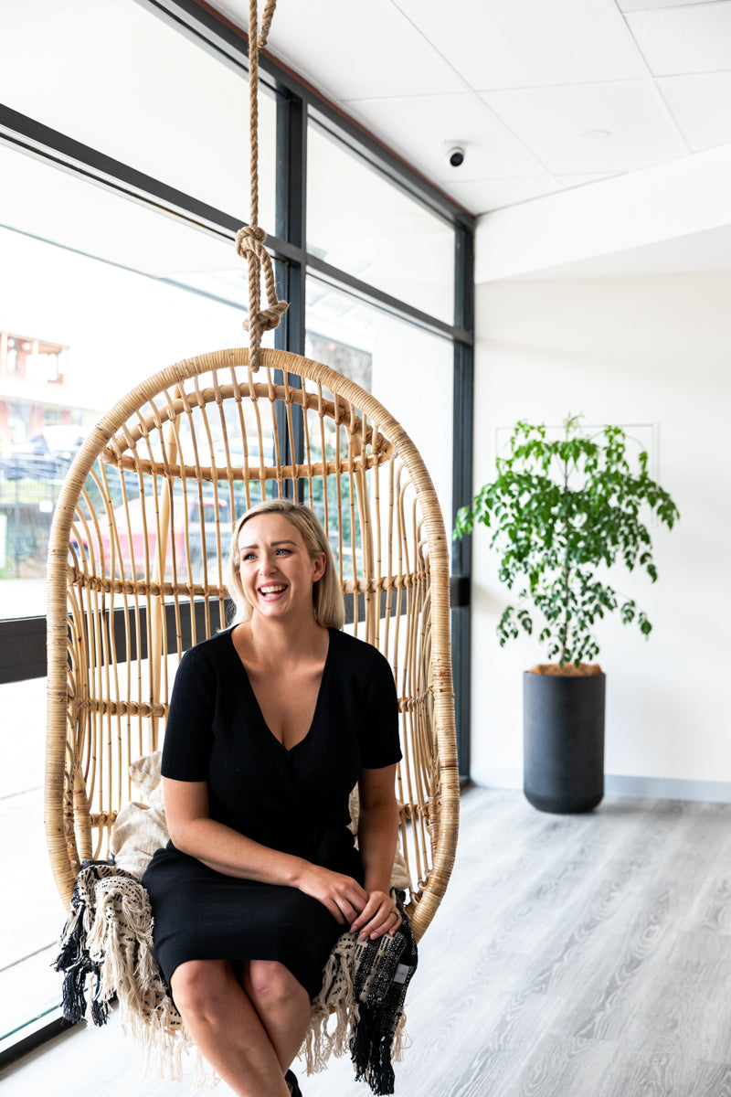 Jacinta sitting on a cane hanging chair. 